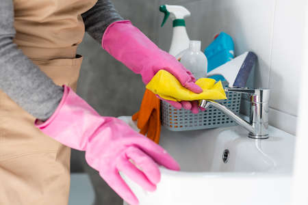 woman doing chores in bathroom at home, cleaning sink and faucet with spray detergent.の写真素材