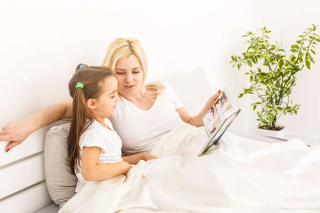 mother and daughter in bed watching a photo bookの写真素材