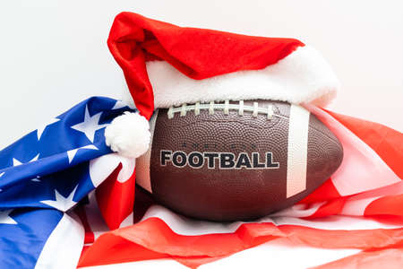 A souvenir ball for rugby or american football in a red santa claus hat on a green background. Preparation for design of tickets, posters, postcards or business cards on the subject of the sports.の写真素材