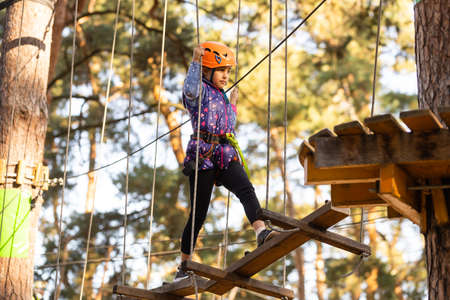 the girl in the orange helmet in the adventure Park holds on to the ropesの写真素材