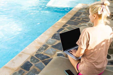 We work even on vacation, Attractive young woman lies on a sun lounger near the pool with a laptop, woman uses a laptop on vacation for work, work onlineの写真素材