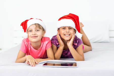 christmas, x-mas, winter, happiness concept - two adorable curly girls playing with tablet pcの写真素材
