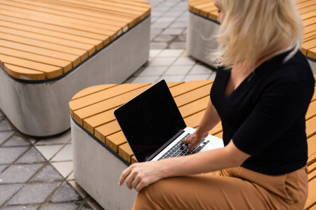 Young woman wearing smartwatch using laptop computer. Female working on laptop in an outdoor cafe.