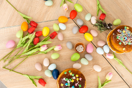 Easter cake with sprinkles, painted eggs and flowers on wooden table, flat lay. Space for text
