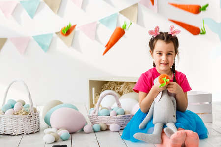 Getting ready to Easter. Lovely little girl holding an Easter egg and smiling with decoration in the backgroundの写真素材