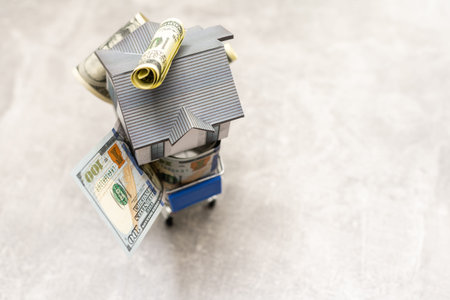House model in mini shopping cart with stack of money on wooden table for residential investment....
