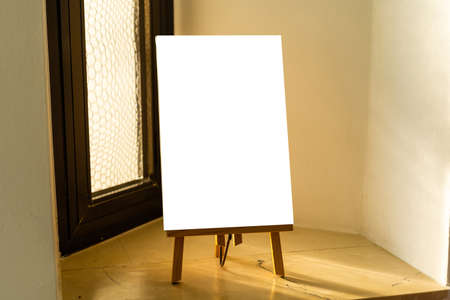 wooden easel with white blank canvas stands near the window in an art studio, prepared for artist work. home activitiesの写真素材