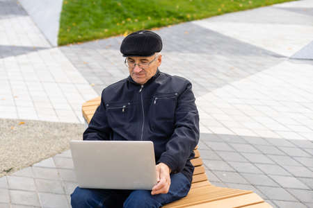 Elderly man use laptop in the park. Handsome senior man in glasses work outside.の写真素材