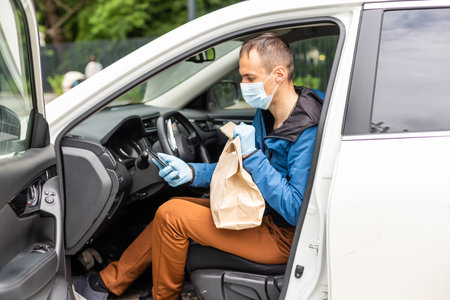 Postal delivery courier man wearing protective face mask in front of cargo van delivering package holding boxの写真素材