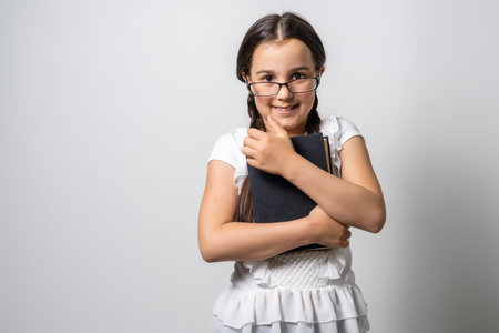 Lovely little girl standing and holding book over white backgroundの写真素材