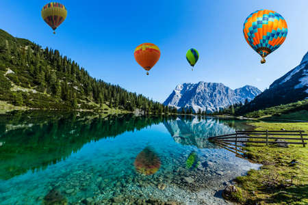 Colorful hot air balloons flying over the lake surrounded by mountains. large multi-colored balloons slowly rising against blue sky. Travel, adventure, festival.の写真素材