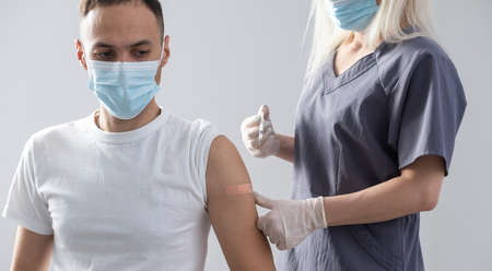 woman doctor in a protective face mask makes vaccination to european man in hospitalの写真素材