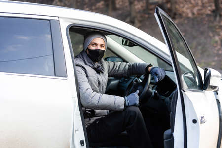 Young adult brunette man in surgical medical mask, jacket posing on city street near the car. Outdoor shot.の写真素材
