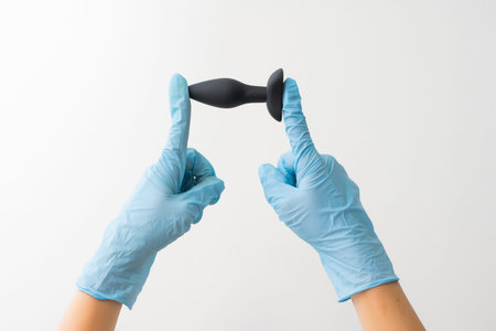 Black butt plug in gloved hand isolated on white