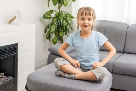 Adorable cute little vlogger looking at webcam, smiling child girl talking to camera making video call vlog communicating online sitting on couch at home, happy preschool kid headshot portrait.の写真素材