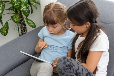 Closeup portrait of two smiling girls lying on couch and using tabletの写真素材