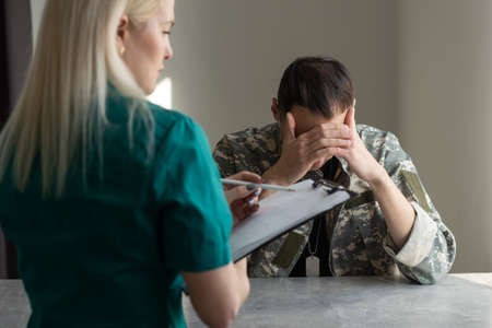 Female doctor and worried military officer discussing about problems he has during psychotherapy treatment.の写真素材