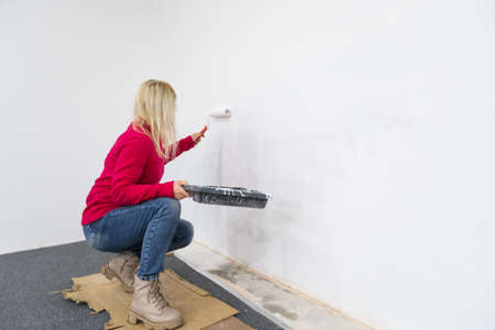 Close up. Side view of pretty joyful Caucasian woman alone painting room in new house in green color. Beautiful female renovating home painting wall using roller brush redesigning apartmentの写真素材