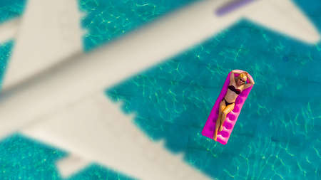 Woman swim on inflatable matrass in the pool and plane over besides travel conceptの写真素材