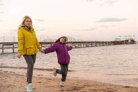 Portrait of mother with her daughter playing near the cold seaの写真素材