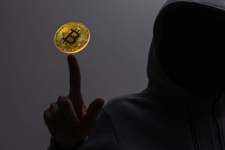 Front view of hacker in blurry interior using computers at desk with creative glowing bitcoin...