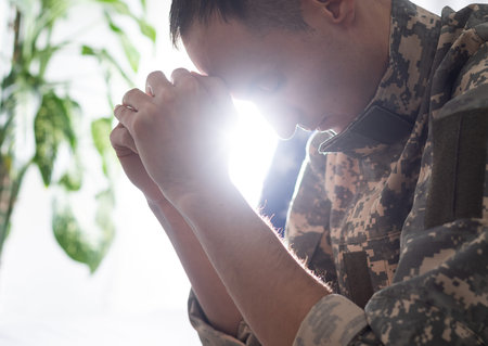sad soldier in camouflage uniform holding military tag in clenched hands