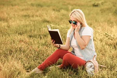 pleased woman in sitting and reading book in park