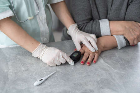 Homehealth care. Woman nurse in a medical mask help middle aged woman during during illness or pressure, female doctor measures the patients pulse and oxygen saturation using a pulse oximeter.の写真素材