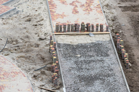 Improvement of the courtyard paving slabs, unfinished work on laying paving slabs. Laid new paving slabs sprinkled with sand and heaps of figured tiles ready for installationの写真素材