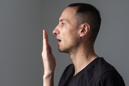 Close up of a good-looking man putting his hand in front of his mouth and checking his bad breathの写真素材