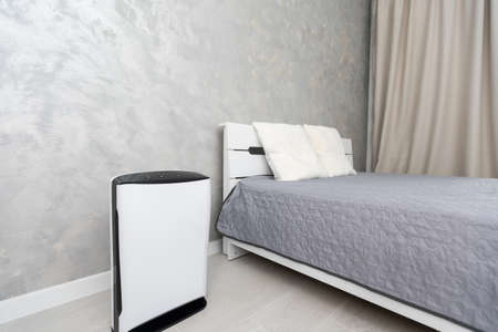 Air purifier in cozy white bedroom for filter and cleaning removing dust PM2.5 HEPA and virus in home for fresh air and healthy Wellness life, Air Pollution Conceptの写真素材