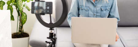 side view of young woman using smartphone at table with laptopの写真素材