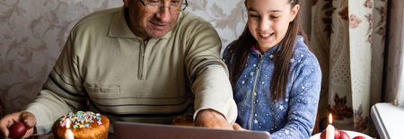 grandfather and granddaughter using laptop on kitchen, online, video call to friends, easter at home...