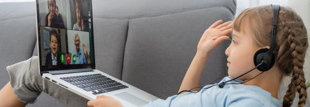 Distance learning. Cheerful little girl girl in headphones using laptop studying through online e-learning system.の写真素材