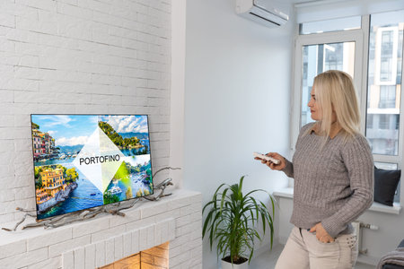 woman relaxing in living room holding remote control and watching television or tv.