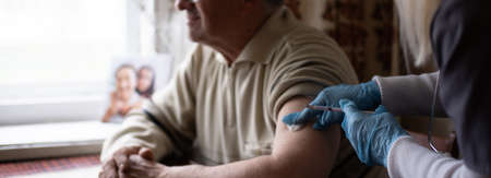 Young woman doctor injecting vaccine to elderly man during home visitの写真素材