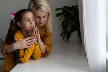 Religious Christian girl and her mother praying at homeの写真素材