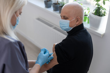 Young woman doctor injecting vaccine to elderly man during home visit