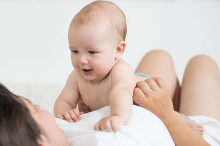 Happy smiling mother and baby lying on bed at homeの写真素材