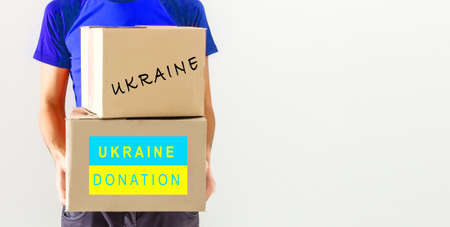 A man holds a box of aid for Ukrainian refugees and poor citizens who find themselves in a war between Ukraine and Russia. Humanitarian aid concept. Donate for refugees.の写真素材