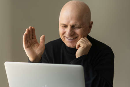 Online teacher with headphones at desk. An elderly man is working on a laptop.の写真素材