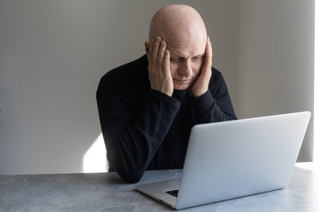 Unhappy depressed senior male sitting at desk with laptop, having frustrated stressed lookの写真素材