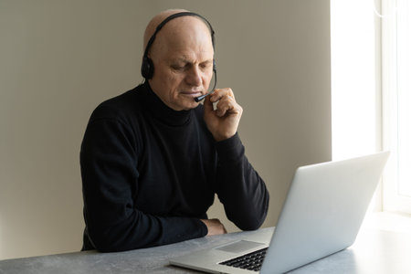 Portrait of grey-haired senior handsome smiling man working from home. Communication online with...