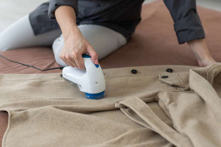 woman uses a machine for removing pellet and spools from clothes and fabric on black trousers. A modern electronic device for updating old thingsの写真素材