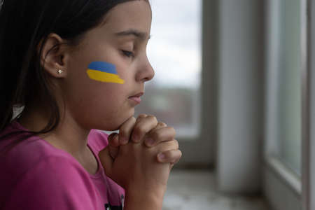 Little girl with Ukrainian flag ribbon praying. Symbol of peace and pray for Ukraine.の写真素材
