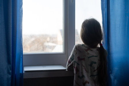 Kids Depression. Unhappy Little Girl Sitting Feeling Lonely Near Window Hugging Herself At Home....