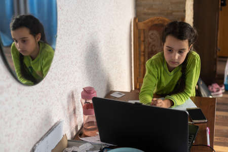 children, education and distant learning concept - little student girl in earphones with laptop computer at home.の写真素材