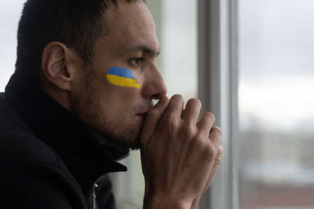 Young sad man with Ukrainian flag symbol on her face crying, stop the war concept, pray for Ukraineの写真素材