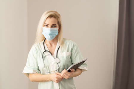 Female Doctor Wearing Scrubs In Hospital Corridor Using Digital Tablet.の写真素材