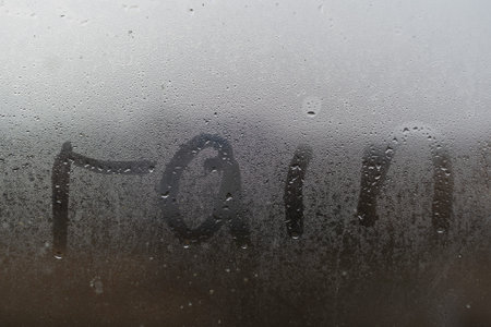 A word Rainy is written on the sweaty foggy window. Water droplets condensation background of dew on...